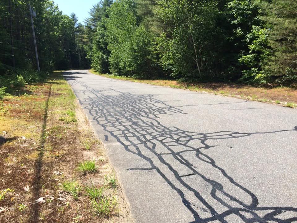 Severe alligator cracking across a rural driveway, hot-rubber fill before full sealcoat