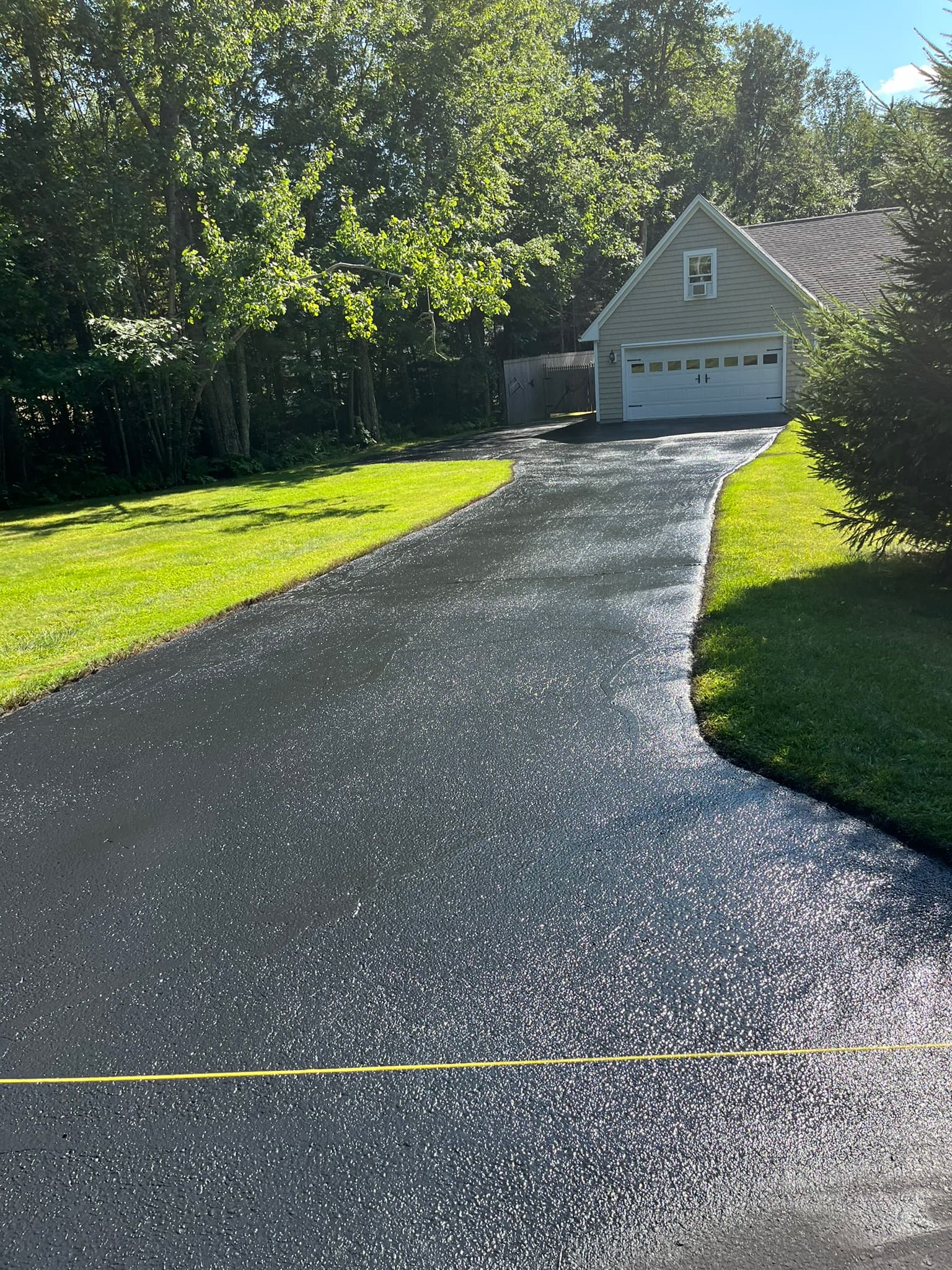 Freshly sealed driveway bordering a lakefront lawn, no runoff onto the grass